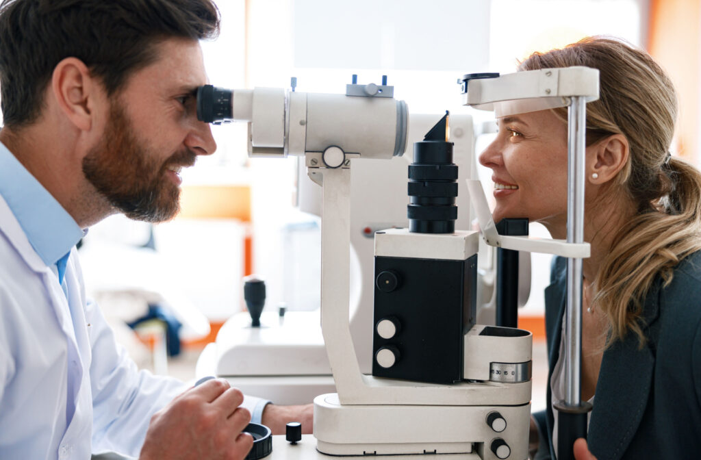An smiling optometrist is conducting an eye exam for a his patient using a slit lamp.