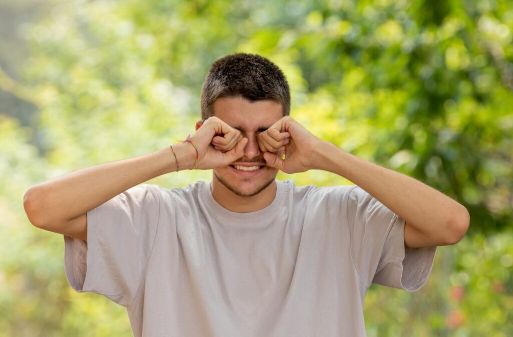 A man rubbing his eyes with both hands outside