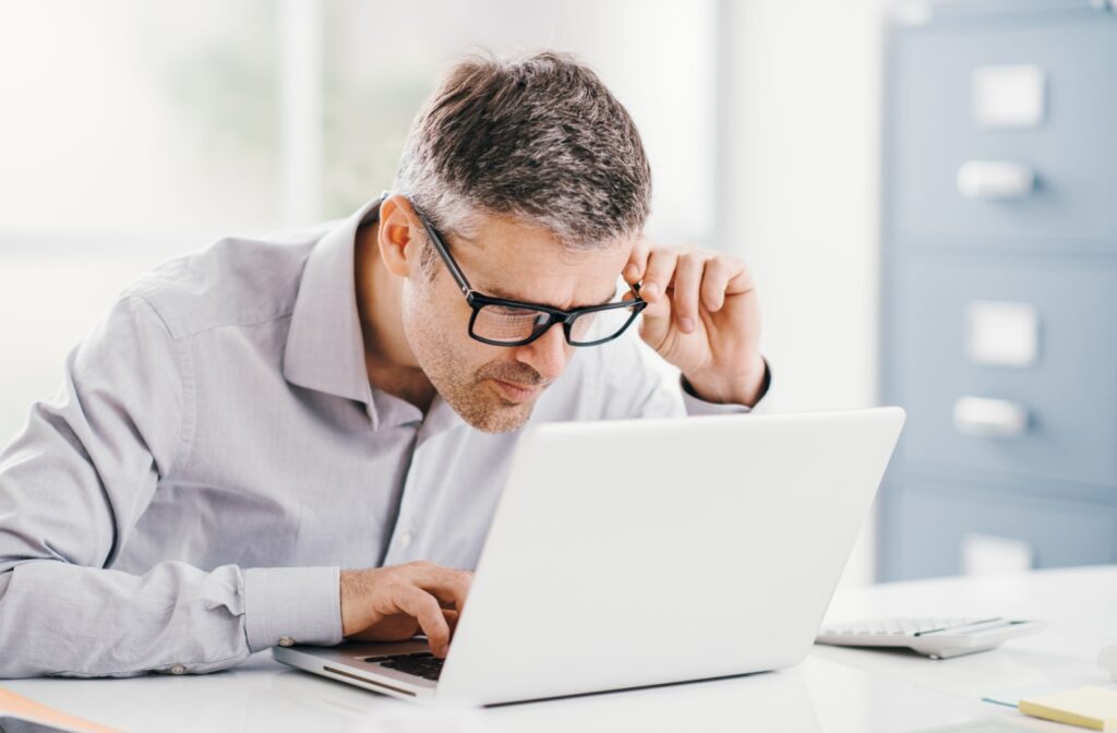 A middle-aged man leaning extremely close to his laptop to see its contents clearly.