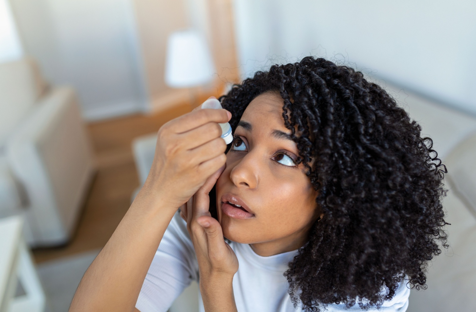 A woman holds one eye open and uses lubricating eye drops to soothe her dry eyes