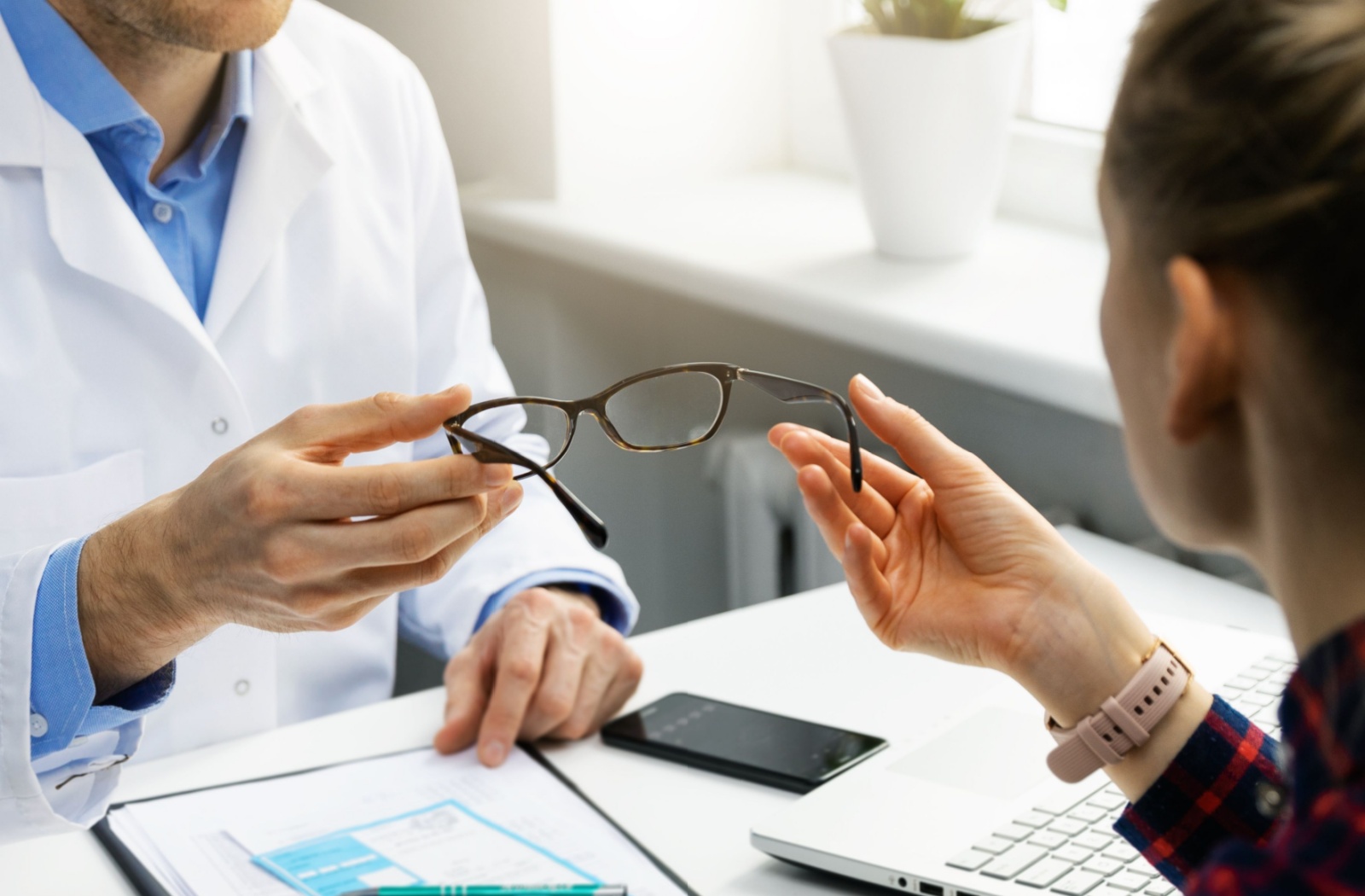 An out-of-frame optometrist handing a patient a new pair of glasses after her comprehensive eye exam.
