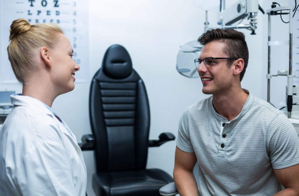 An optometrist explains the results of an eye exam to their patient in a clean, white examination room.
