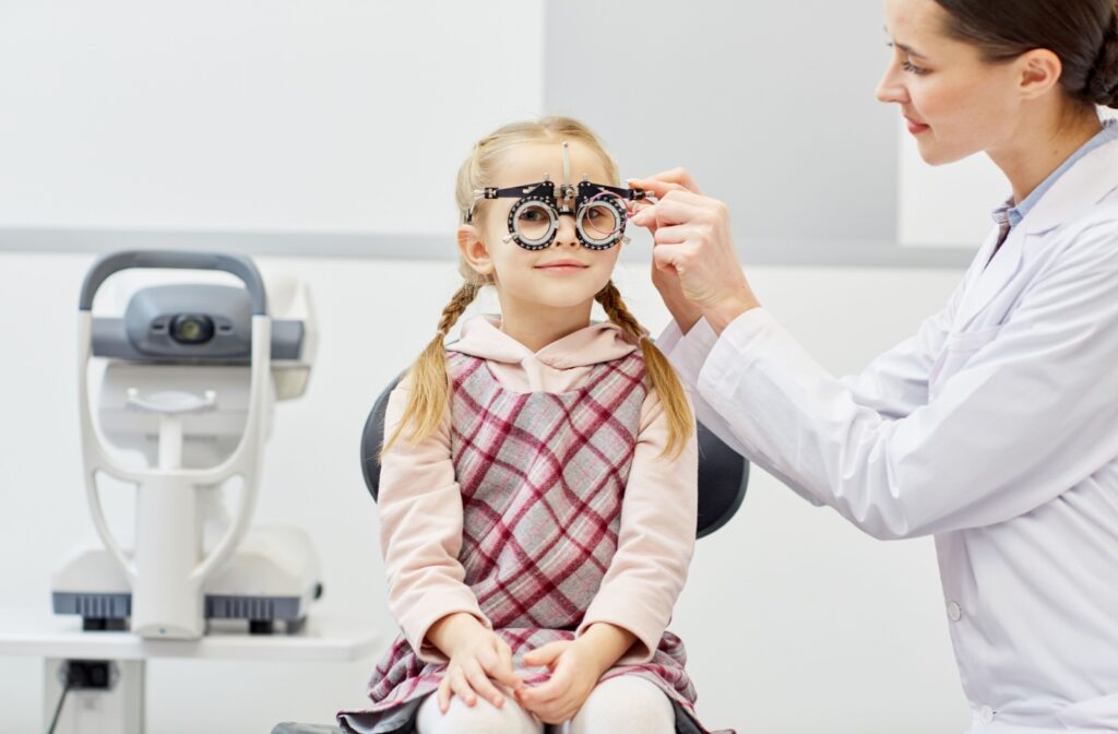 A child sits in an exam chair wearing a trial frame while an optometrist adjusts the lenses during an eye exam.