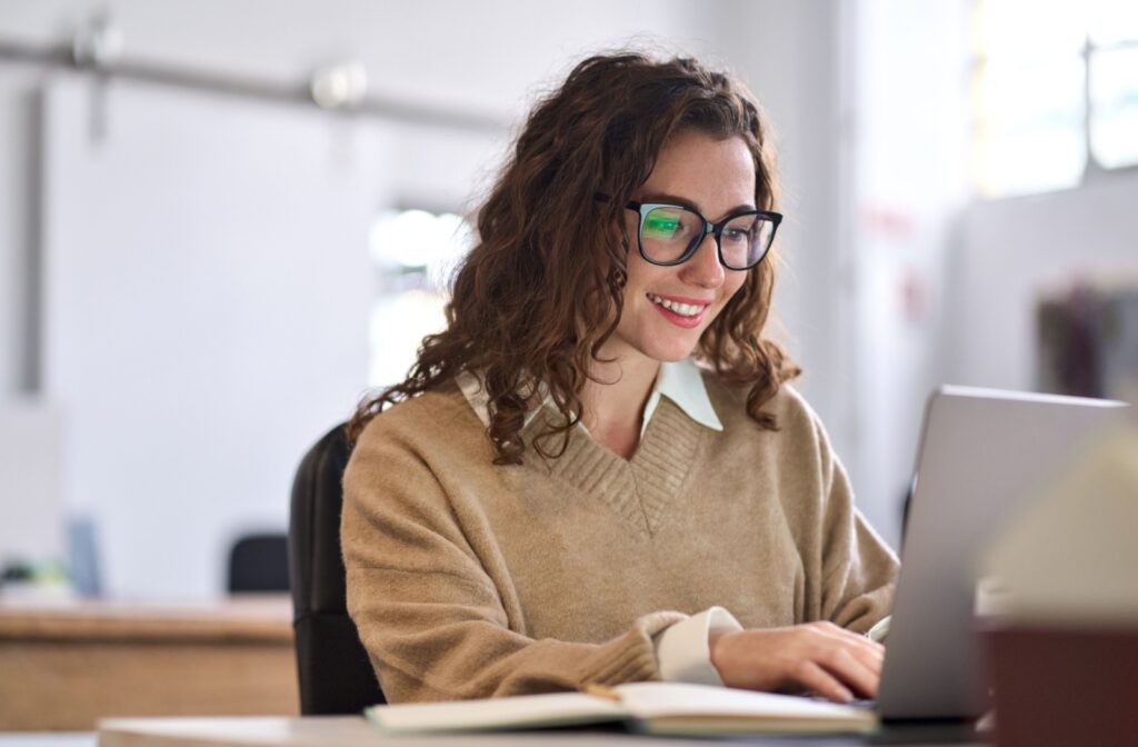 A woman sits in front of the computer while using glasses to prevent digital eye strain