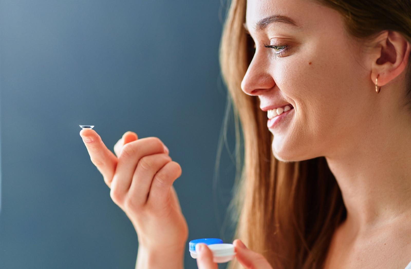 A person looking up closely at a contact lens that is resting on their finger