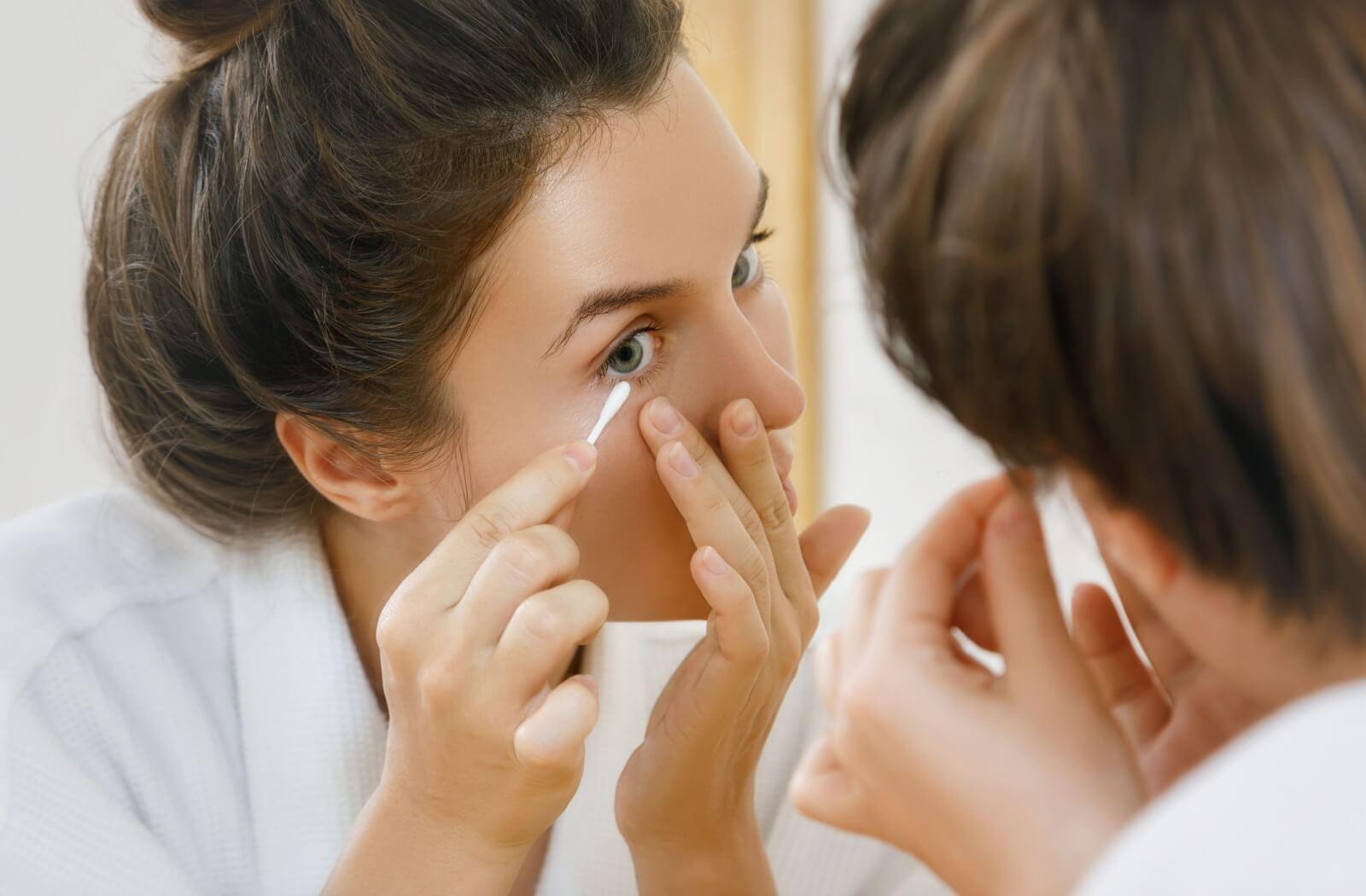 A person using a q-tip on their eye to help remove makeup